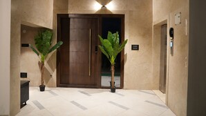 A lobby with a marble floor, a wooden door, and two potted plants.