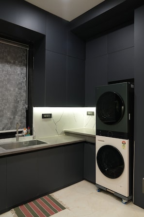 A compact kitchen with a built-in washer and dryer, a sink, and a marble backsplash. - Luxury 2BHK Westside Penthouse, Private Patio & Terrace HiTech City Madhapur HYD (Hyderabad)