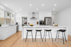 Une cuisine moderne avec des meubles blancs, une hotte en acier inoxydable et un îlot central doté de tabourets.
