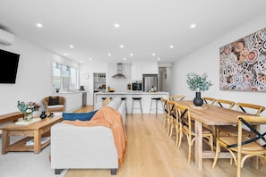 Una cocina moderna con armarios blancos, una isla central y un comedor con sillas y una mesa de madera.