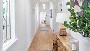 Ein Flur mit Holzboden, einem grauen Teppich, einer Holzbank, einem Tisch mit Lampe, einer Topfpflanze und einem farbenfrohen abstrakten Gemälde an der Wand.