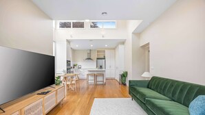 A modern living room with a flat-screen TV, a green sofa, and a dining area with wooden furniture. - Character-Filled, Modern Retreat In Mount Pleasant, Ballarat (Mount Pleasant)