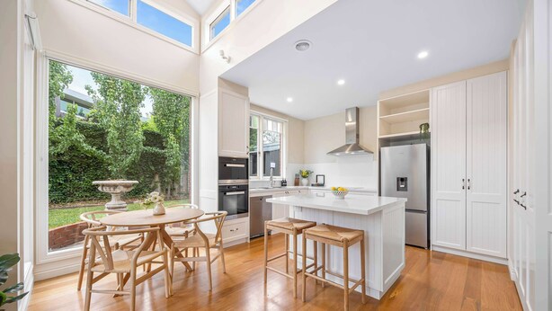 A modern kitchen with white cabinetry, a central island, and a dining area with wooden chairs. - Character-Filled, Modern Retreat In Mount Pleasant, Ballarat (Mount Pleasant)
