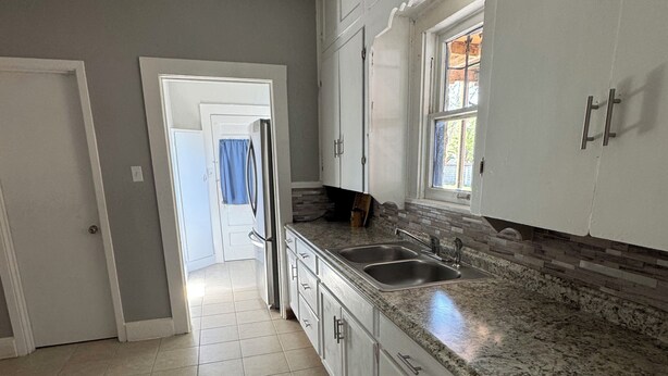 A kitchen with white cabinets, a granite countertop, a stainless steel sink, and a window with blinds.