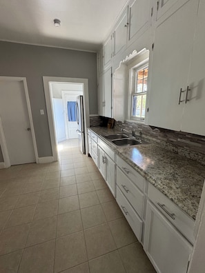 A kitchen with white cabinets, a granite countertop, a stainless steel sink, and a window with blinds.