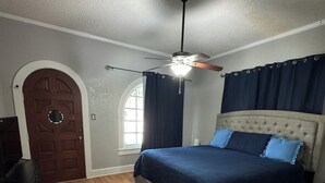 A bedroom with a bed, a ceiling fan, a wooden dresser, and a door.