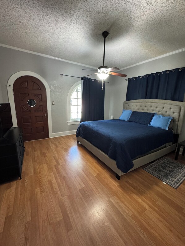 A bedroom with a bed, a ceiling fan, a wooden dresser, and a door.