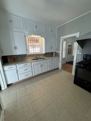 A kitchen with white cabinets, a granite countertop, a black stove, and a window with barred glass. - Downtown stay with games, coffee and spacious rooms (Del Rio)