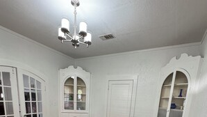 A dining room with a wooden table, four chairs, a chandelier, and white walls with decorative moldings.