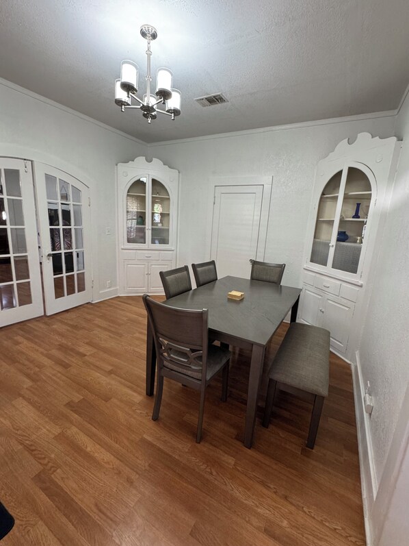 A dining room with a wooden table, four chairs, a chandelier, and white walls with decorative moldings. - Downtown stay with games, coffee and spacious rooms (Del Rio)