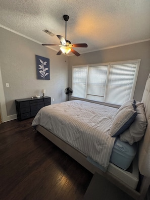 A bedroom with a bed, a ceiling fan, a nightstand, a lamp, and a wall-mounted artwork.