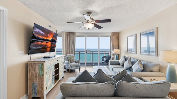 Een woonkamer met een televisie, bank en een balkon met uitzicht op zee.