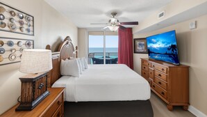 Een hotelkamer met een bed, een televisie, een dressoir, een lamp en uitzicht op zee.