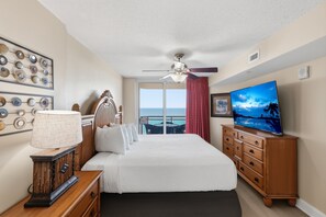 A hotel room with a bed, a TV, a dresser, a lamp, and a view of the ocean. - Bahama Sands 1203 | Breathtaking Oceanfront Condo with Pools & Hot Tub (North Myrtle Beach)