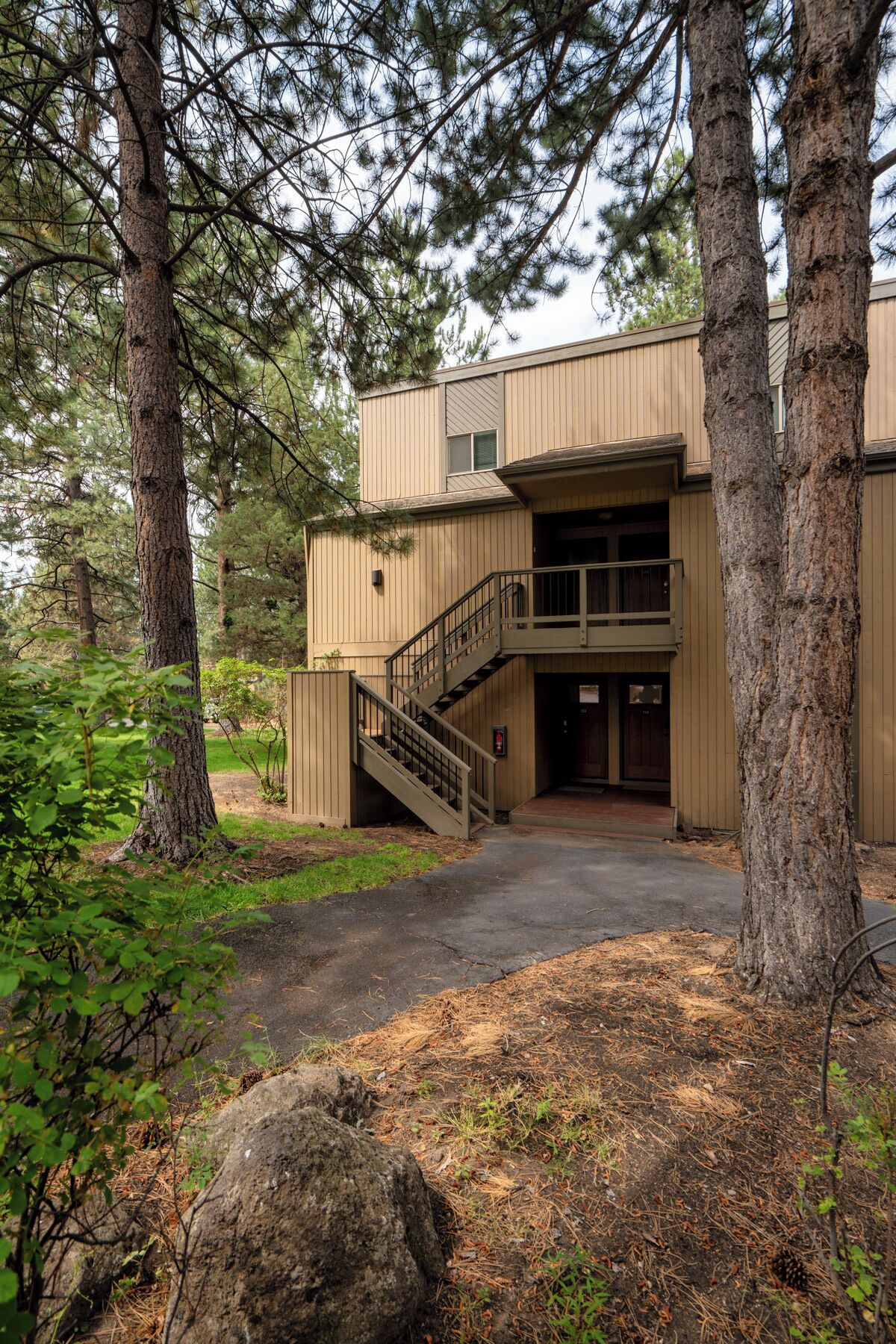 A two-story building with a staircase leading to the entrance, surrounded by trees and a stone pathway.