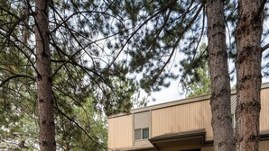 A two-story building with a staircase leading to the entrance, surrounded by trees and a stone pathway. - Mountain Modern Condo + Resort Amenities & Patio (Bend)