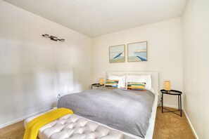 Een slaapkamer met een bed, nachtkastjes, een bankje en twee kunstwerken aan de muur.