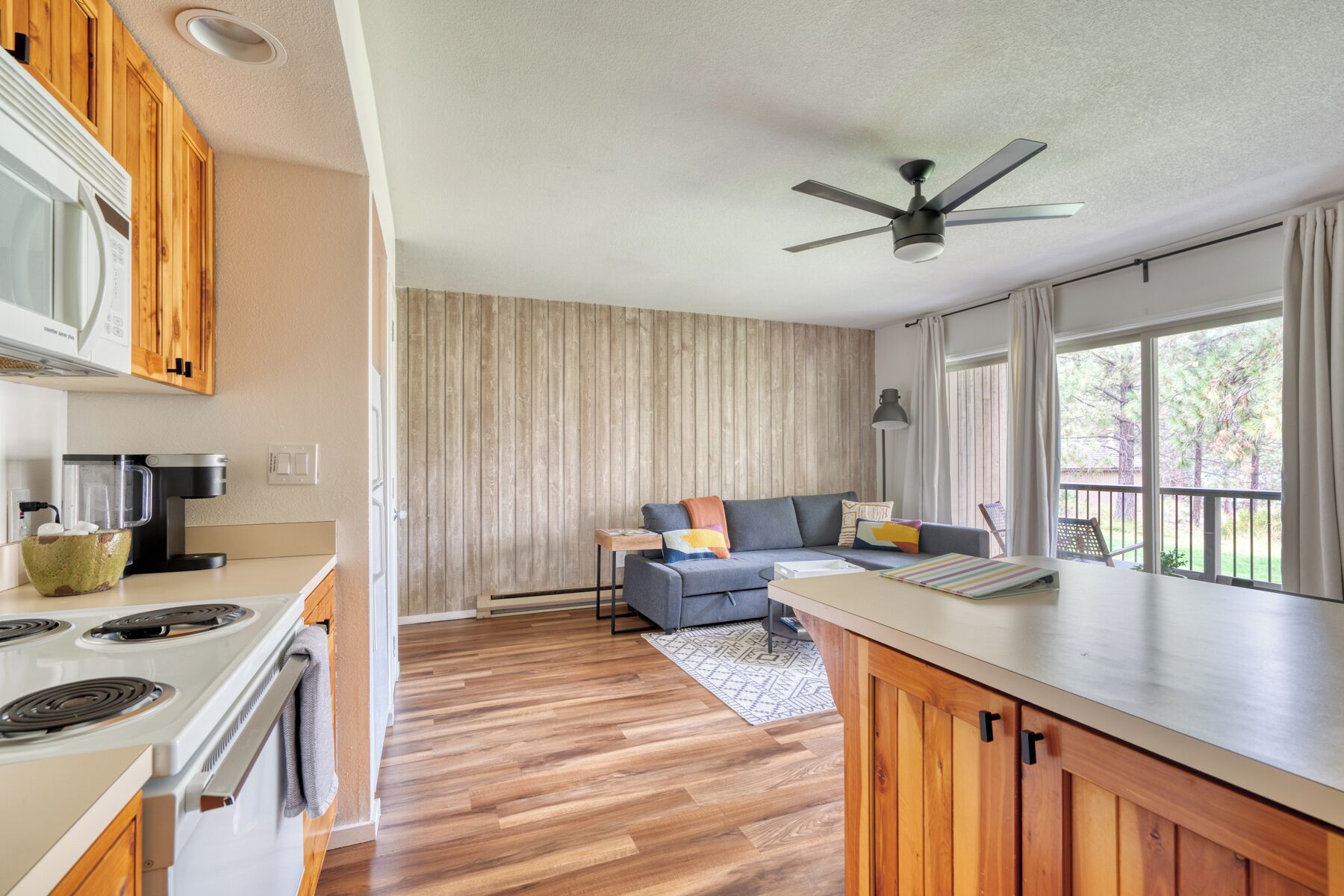 A modern kitchen with a stove, a coffee maker, and a dining area with a sofa and a table.