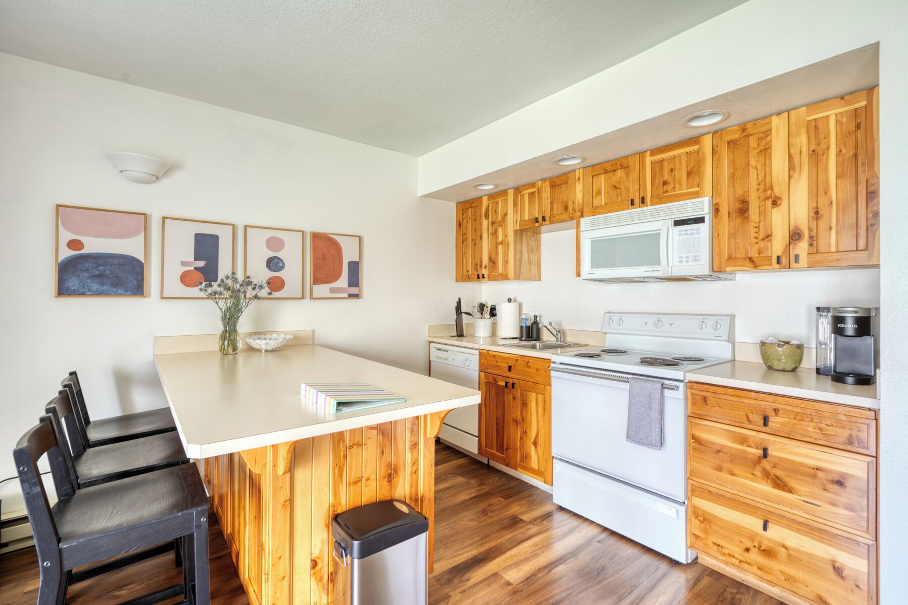 A modern kitchen with wooden cabinets, a white countertop, a built-in microwave, a stove, and a sink.