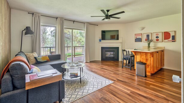 A living room with a sofa, a coffee table, a fireplace, and a dining area with a bar. - Mountain Modern Condo + Resort Amenities & Patio (Bend)