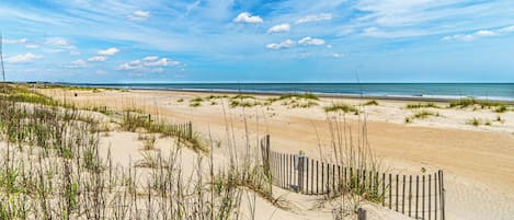 A sandy beach with a wooden fence and sparse vegetation.