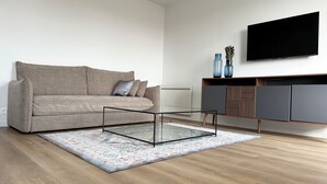 Een woonkamer met een bank, een glazen salontafel, een televisie en een kast.
