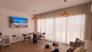 Un salón moderno con comedor, piso de madera y un amplio ventanal con cortinas.