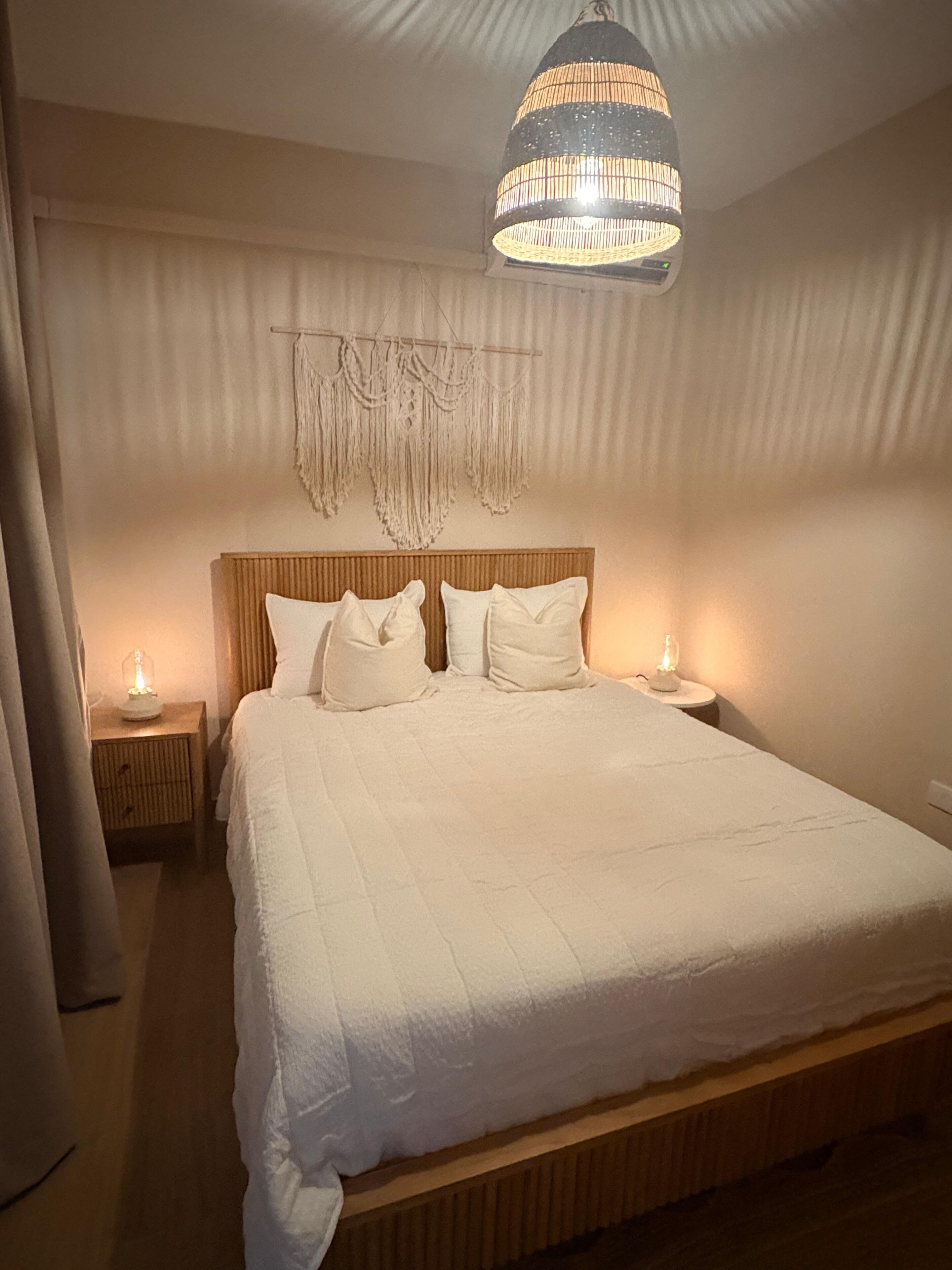 Een slaapkamer met een groot bed, houten hoofdbord, bedlampjes en een hangende lamp.