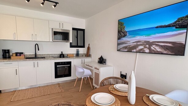 Una cocina moderna con armarios blancos, un microondas y un comedor con una mesa de madera dispuesta para cuatro.