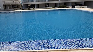Un hotel moderno con piscina, varios balcones y cielo despejado.