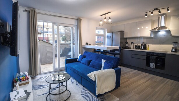 Una sala de estar moderna con un sofá azul, una mesa de centro y una cocina con estufa, lavabo y armarios.