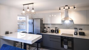 Una cocina moderna con encimera blanca, taburetes de bar, horno integrado, cafetera y hervidor.