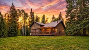 Eine Blockhütte mit Veranda, umgeben von einer Wiese und hohen Bäumen.