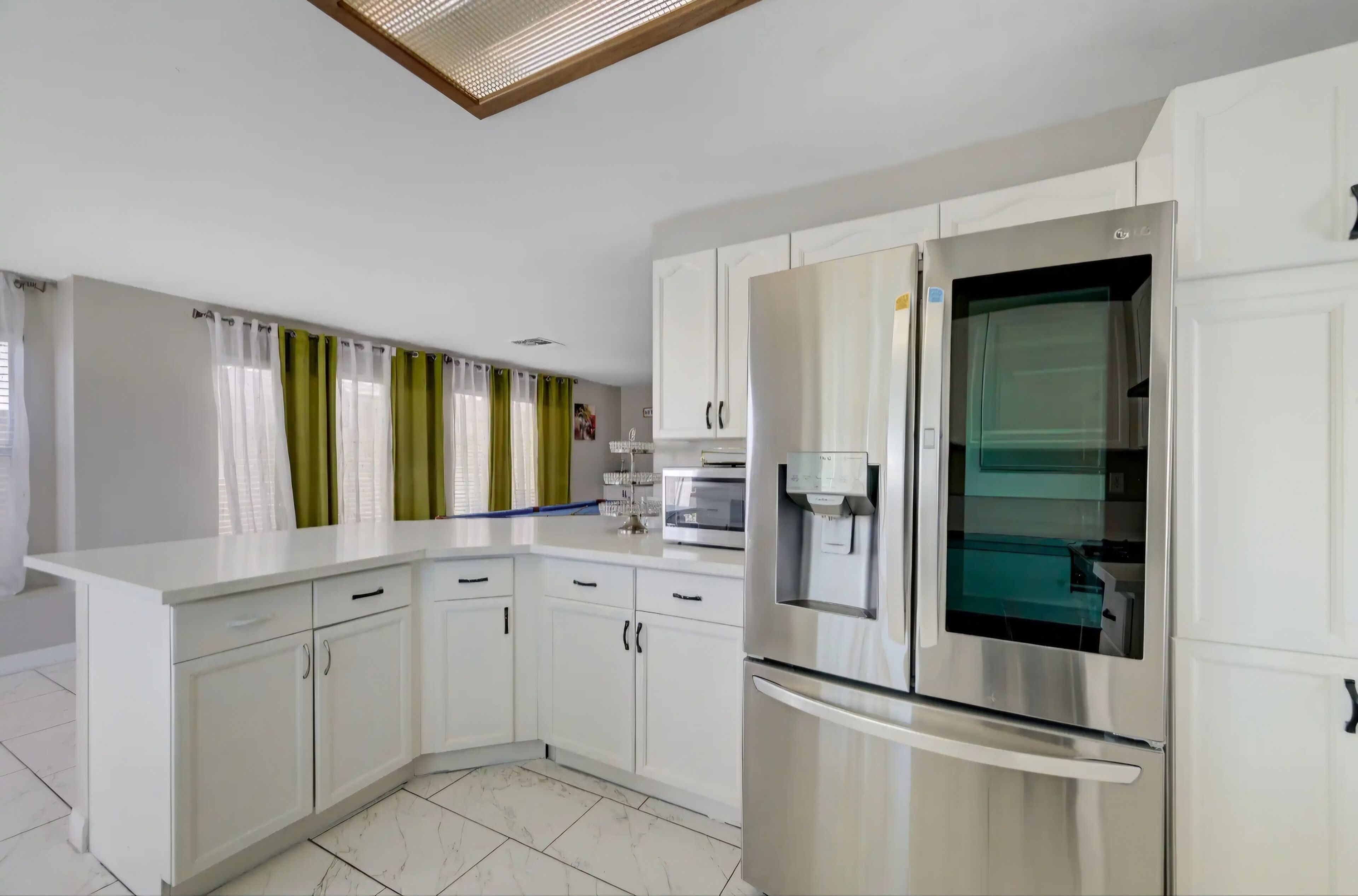Una cocina moderna con armarios blancos, un refrigerador de acero inoxidable y un horno empotrado.