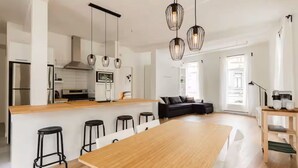 Et moderne køkken med en central ø, barstole, hængende lamper og et spiseområde med et stort bord.