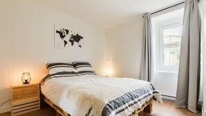 Ein Schlafzimmer mit einem hölzernen Bett, einer Weltkarte an der Wand, einer Nachttischlampe und einem Fenster mit Vorhängen.