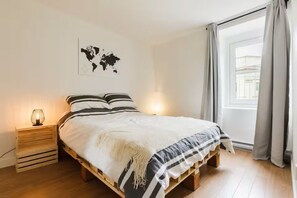 Quarto com cama de madeira, mapa mundi na parede, abajur e janela com cortinas.