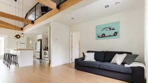 Ein modernes Interieur mit einem dunkelgrauen Sofa, Holzbalken, einer Kücheninsel und einer Wandillustration mit einem türkisfarbenen Auto.