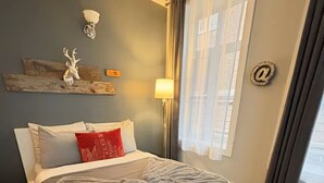 A bedroom with a bed, a wall-mounted light, a window with curtains, and a decorative wall piece. - Urban loft | Rue Saint-Joseph (Québec)