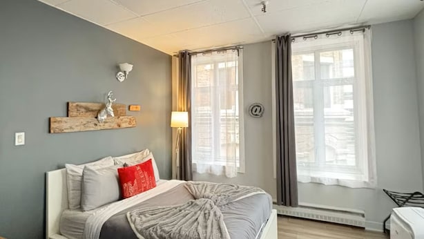 A bedroom with a bed, a desk, a heater, and a window with curtains. - Urban loft | Rue Saint-Joseph (Québec)