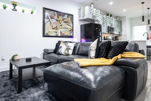 Een moderne woonkamer met een zwarte leren bank, een bijzettafeltje en een schilderij aan de muur.