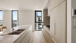 A modern kitchen with a large island, built-in appliances, and a view through an open door. - Yves Residences - 2204 (Mermaid Beach)