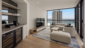 A modern living room with a large TV, comfortable seating, a coffee bar, and a view of the ocean. - Yves Residences - 2204 (Mermaid Beach)