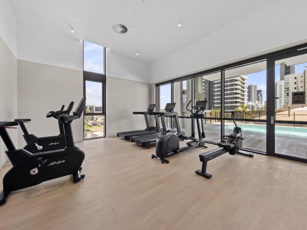 Ein Fitnessraum mit Cardiogeräten, großen Fenstern und Blick auf Gebäude sowie einen Pool.