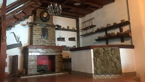 A rustic interior with a brick fireplace, wooden beams, and shelves with pottery.