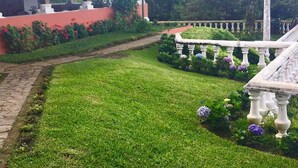 A garden with a pathway, a white balustrade, and a building with a red wall.