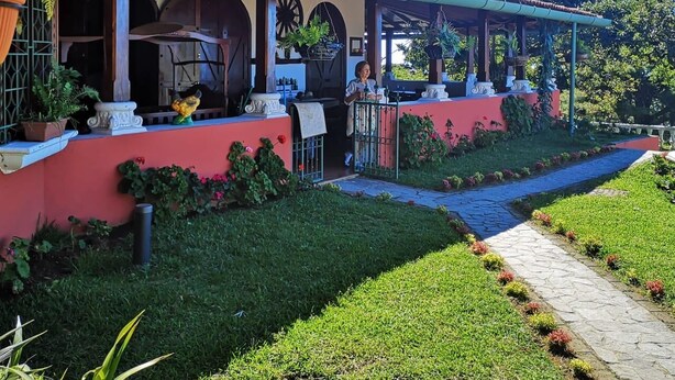 A red building with a covered patio, a window, and a pathway leading to a garden.