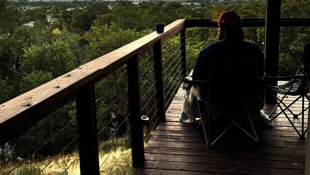 Una terraza de madera con barandilla que da a un paisaje con árboles y montañas lejanas.