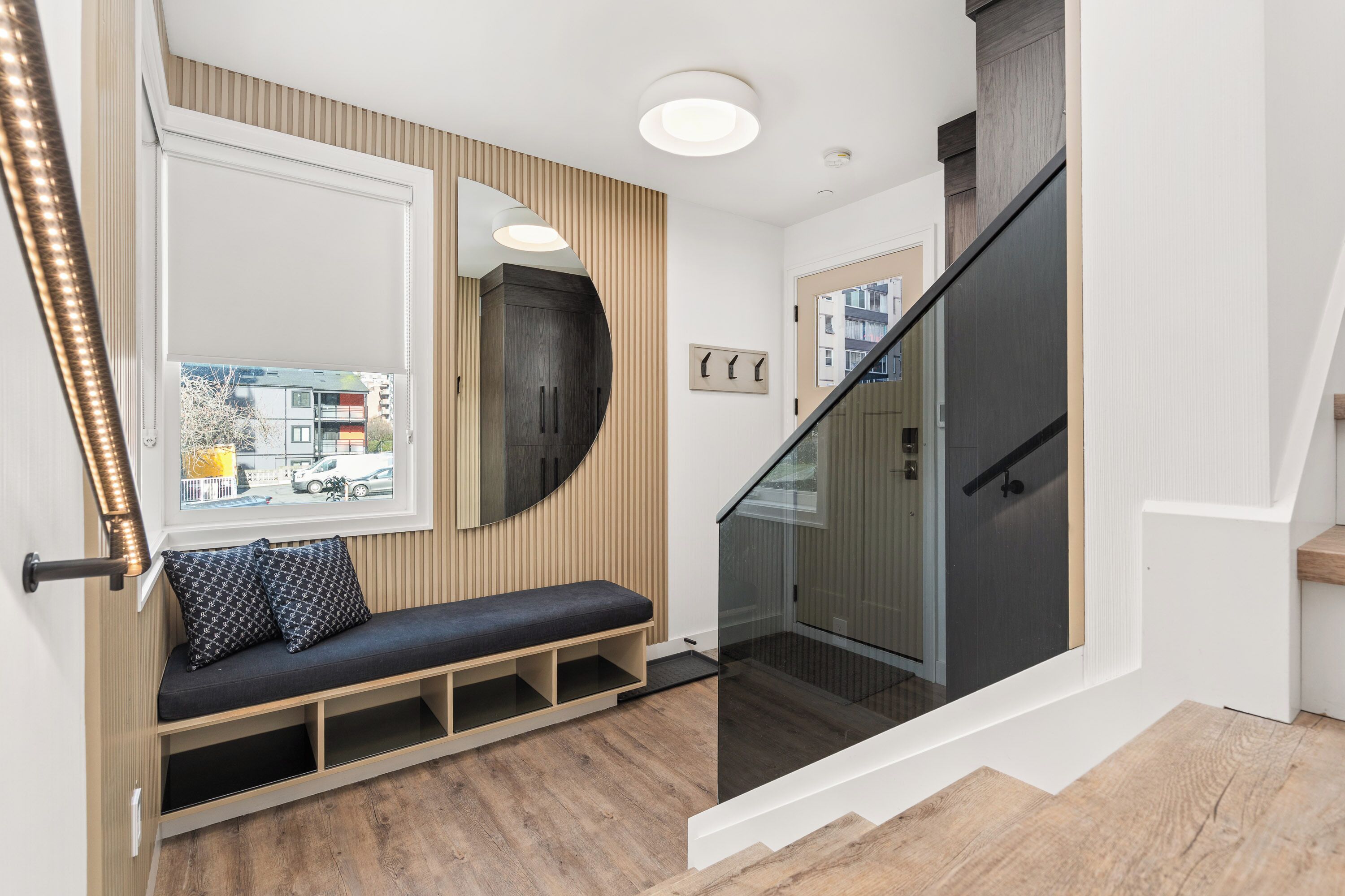 A modern interior with a bench, a mirror, a staircase, and a view of the outside.