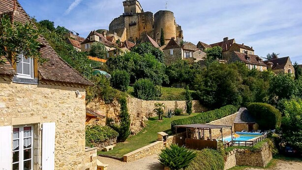 A historic stone building with a courtyard, a pool, and a castle in the background. - Charmante maison avec piscine (Castelnaud-la-Chapelle)